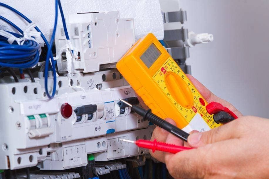 Hands Using a Yellow Multimeter to Test Voltage on a Complex Circuit Board