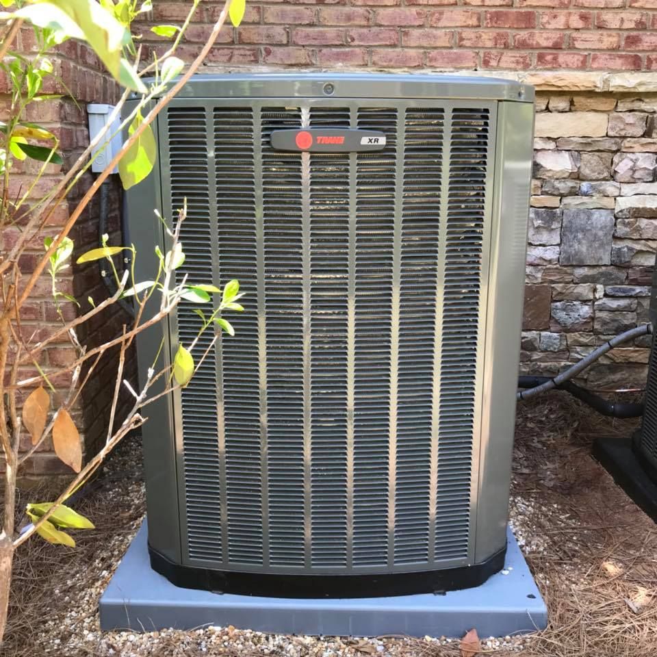 A large air conditioner is sitting outside of a brick building.