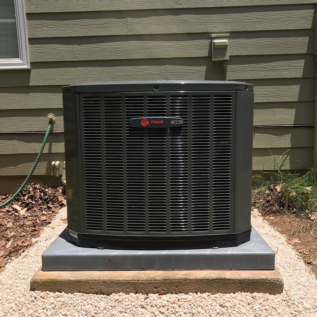 Air Connections Inc - An air conditioner is sitting on top of a gravel platform in front of a house.