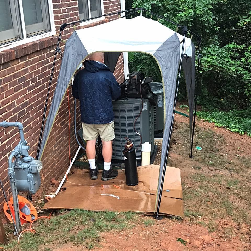 Air Connections Inc - A man is working on an air conditioner under a tent.