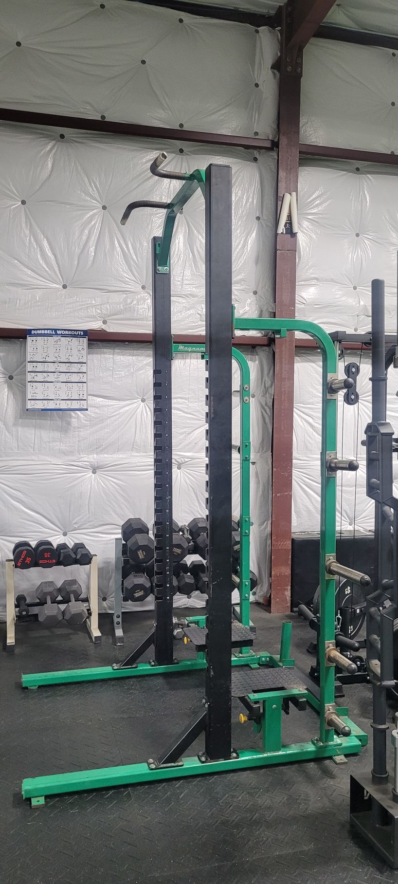 A green and black squat rack is sitting in a gym.