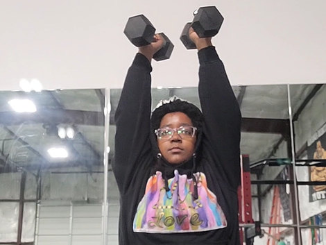 A woman in a black hoodie is lifting dumbbells over her head in a gym  - Odenton , MD - Fitness Forever