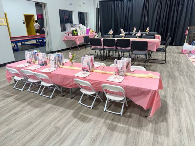 Party tables set with pink tablecloths, chairs, and decorations in a gymnasium.