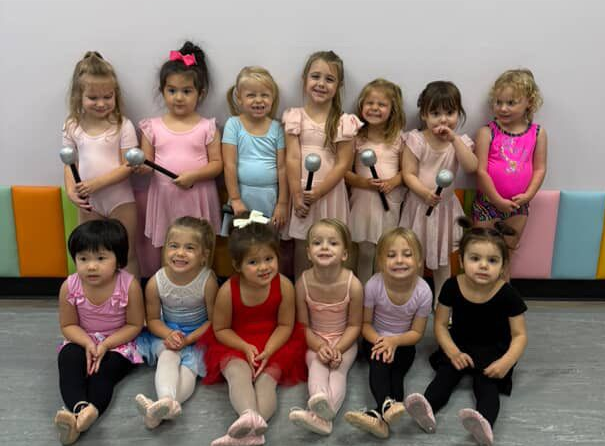 Young dancers in colorful leotards holding microphones, posing together indoors.