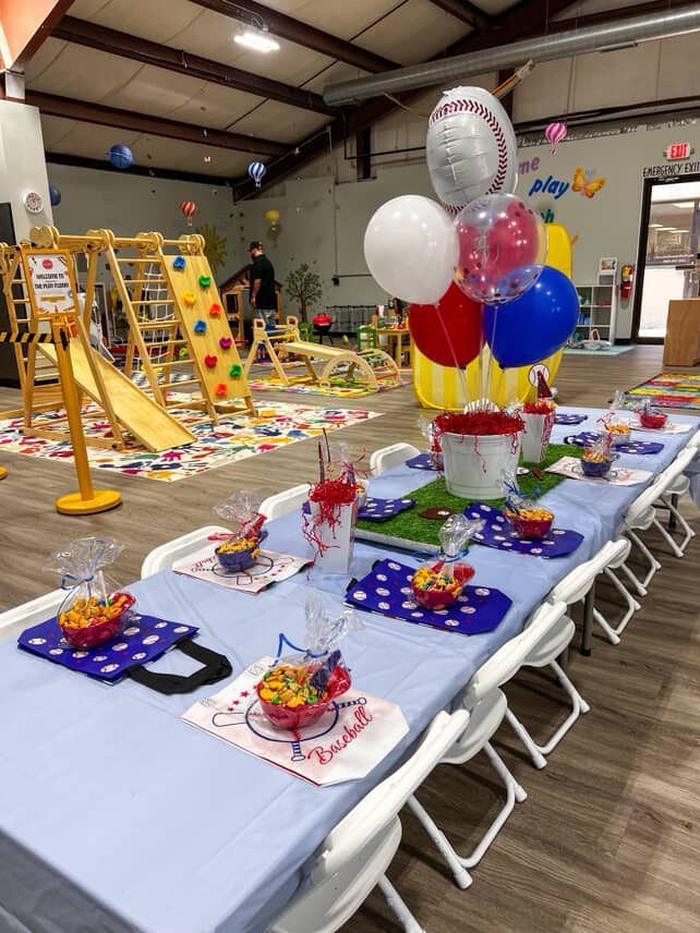 Birthday party table set up in a children's play area with balloons and snacks.