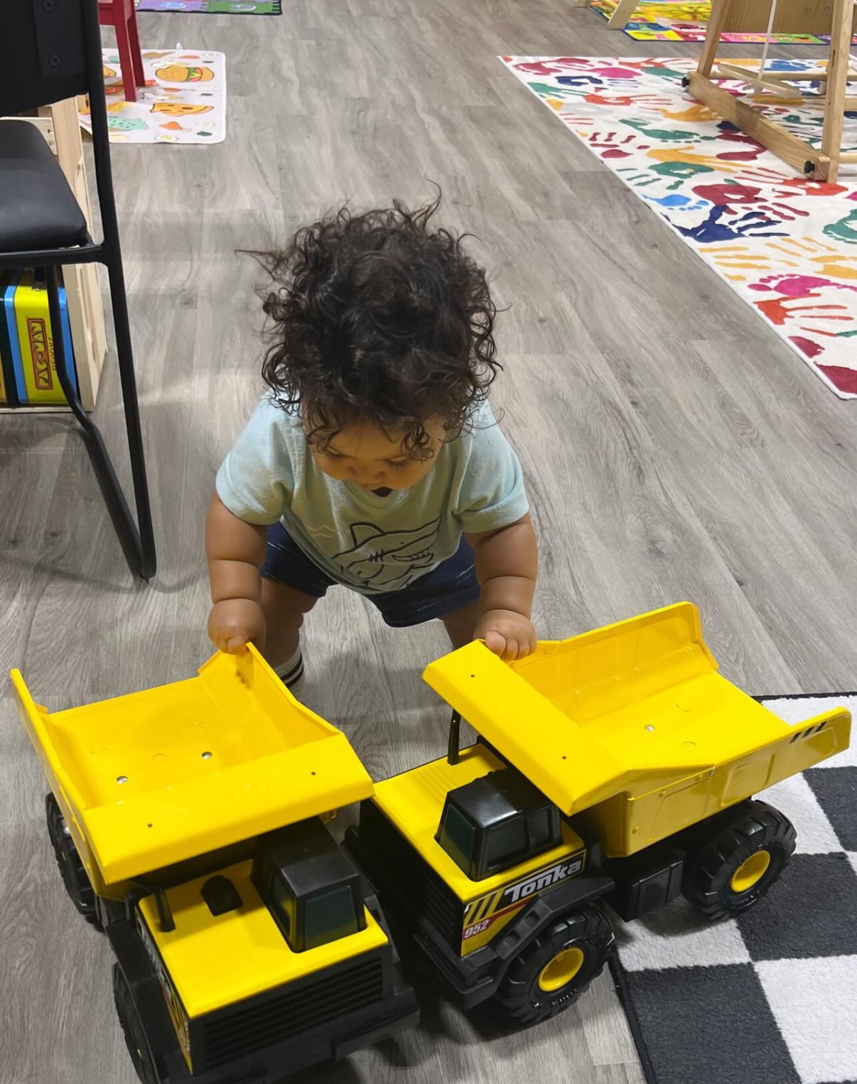 Child playing with two yellow toy dump trucks on a checkered rug.