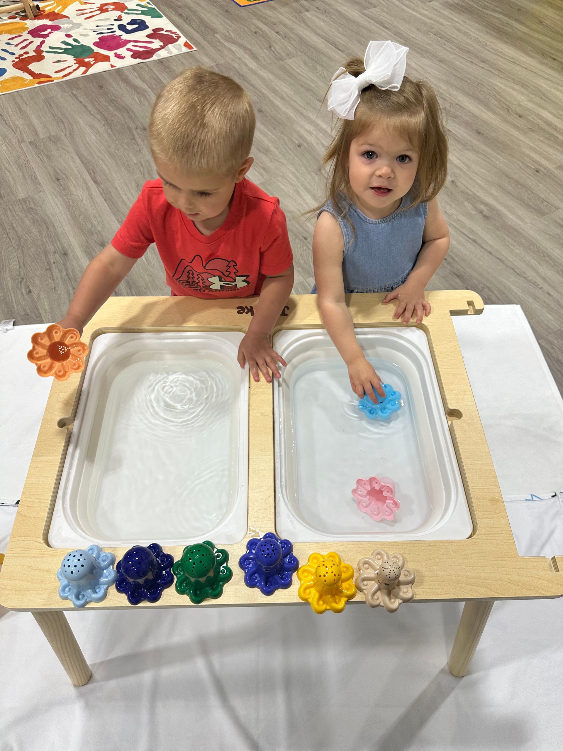 Two children playing in water bins at a table. They are using colorful flower toys.