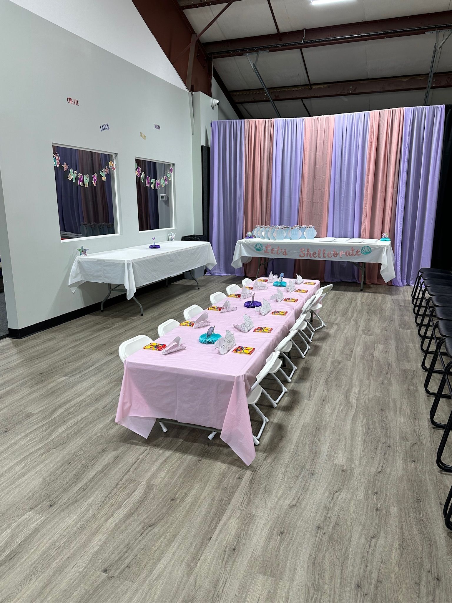 Party room with tables set for an event; draped backdrop in pink and purple.