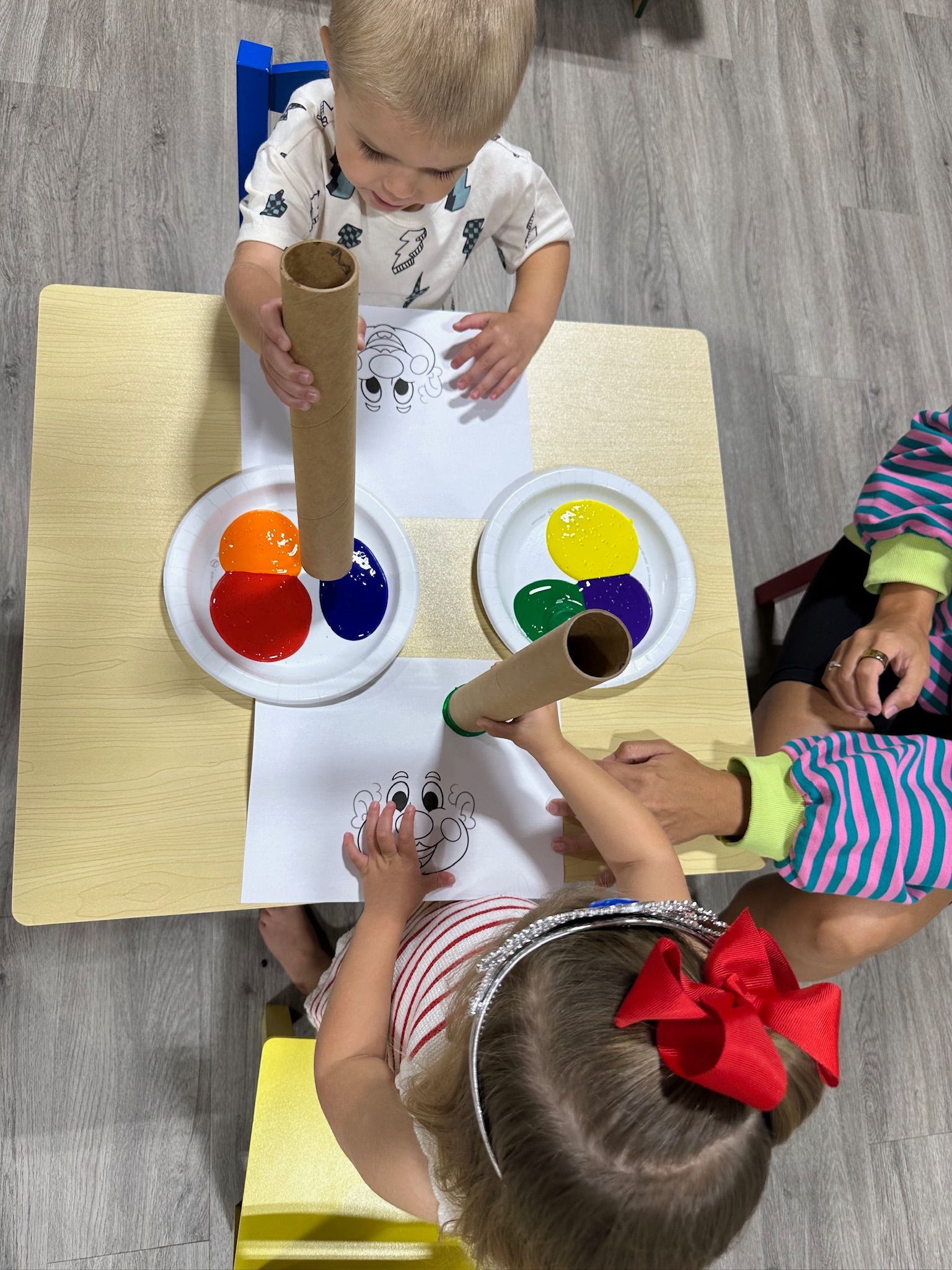 Children paint with tubes, using color palettes on a table.