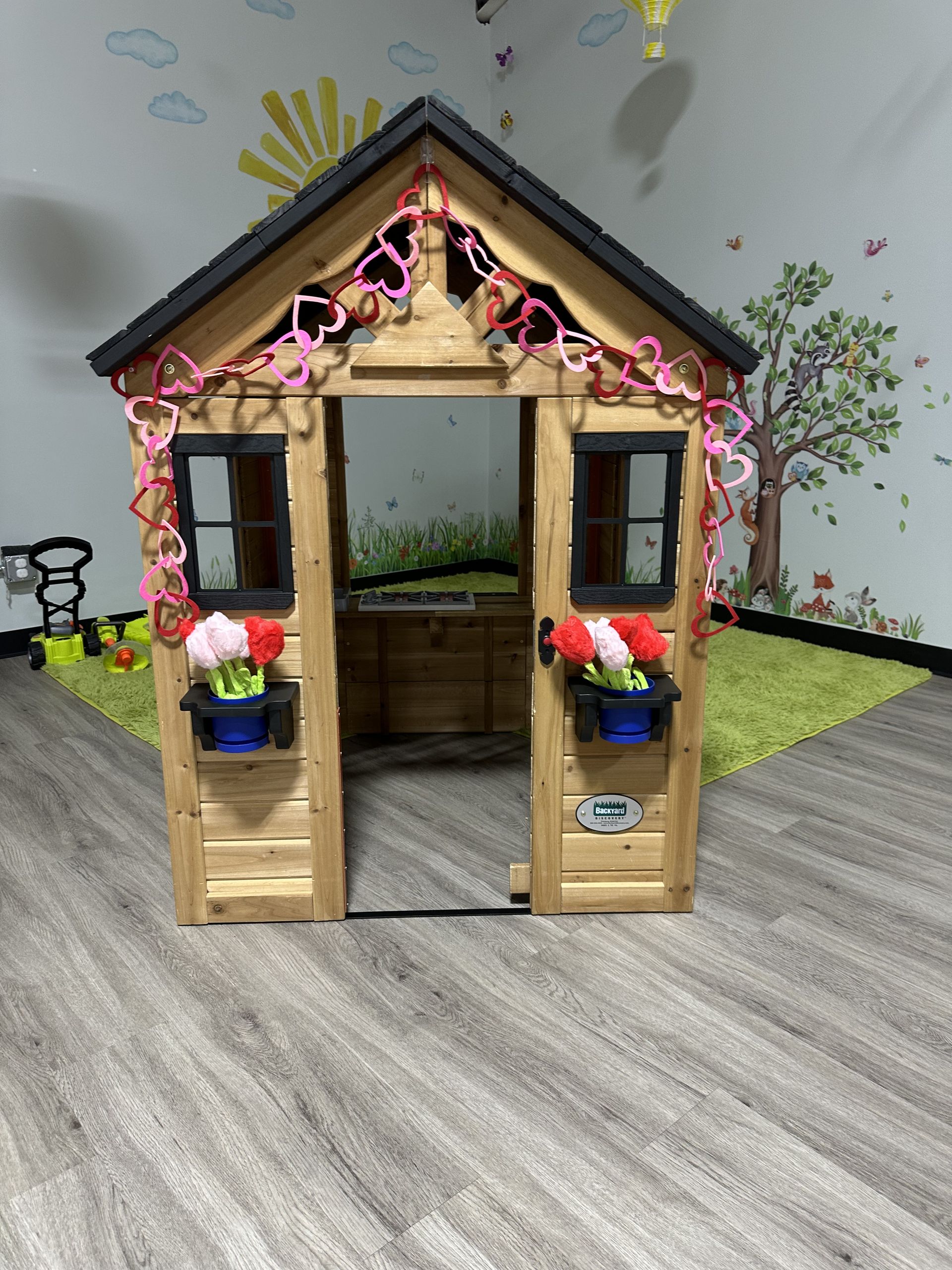 Wooden playhouse decorated with hearts and flowers, with open doorway and windows.