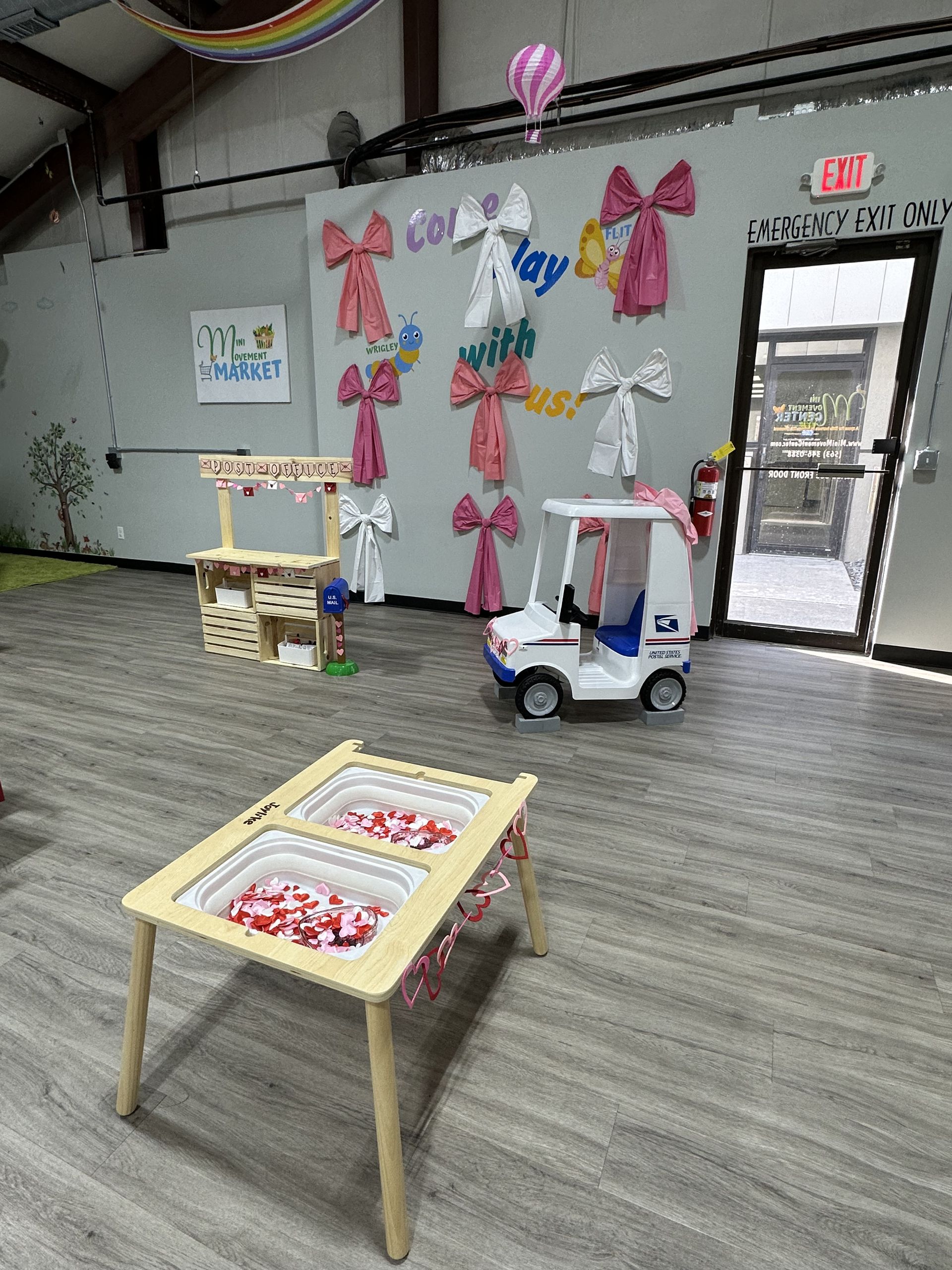 Playroom with toy booth, mail truck, and bow decorations on a wall.