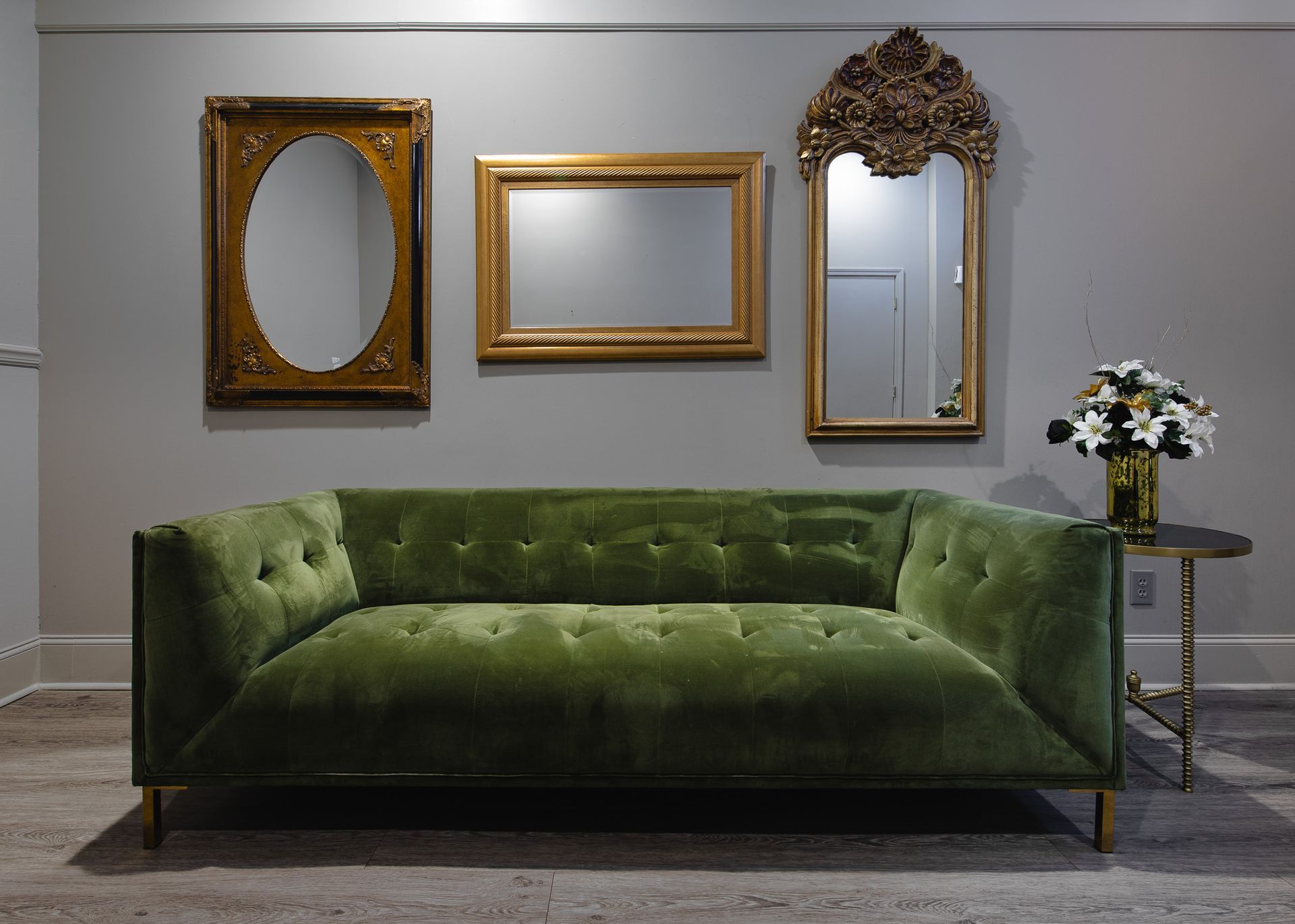 green plush fainting couch and three vintage mirrors hanging on wall above