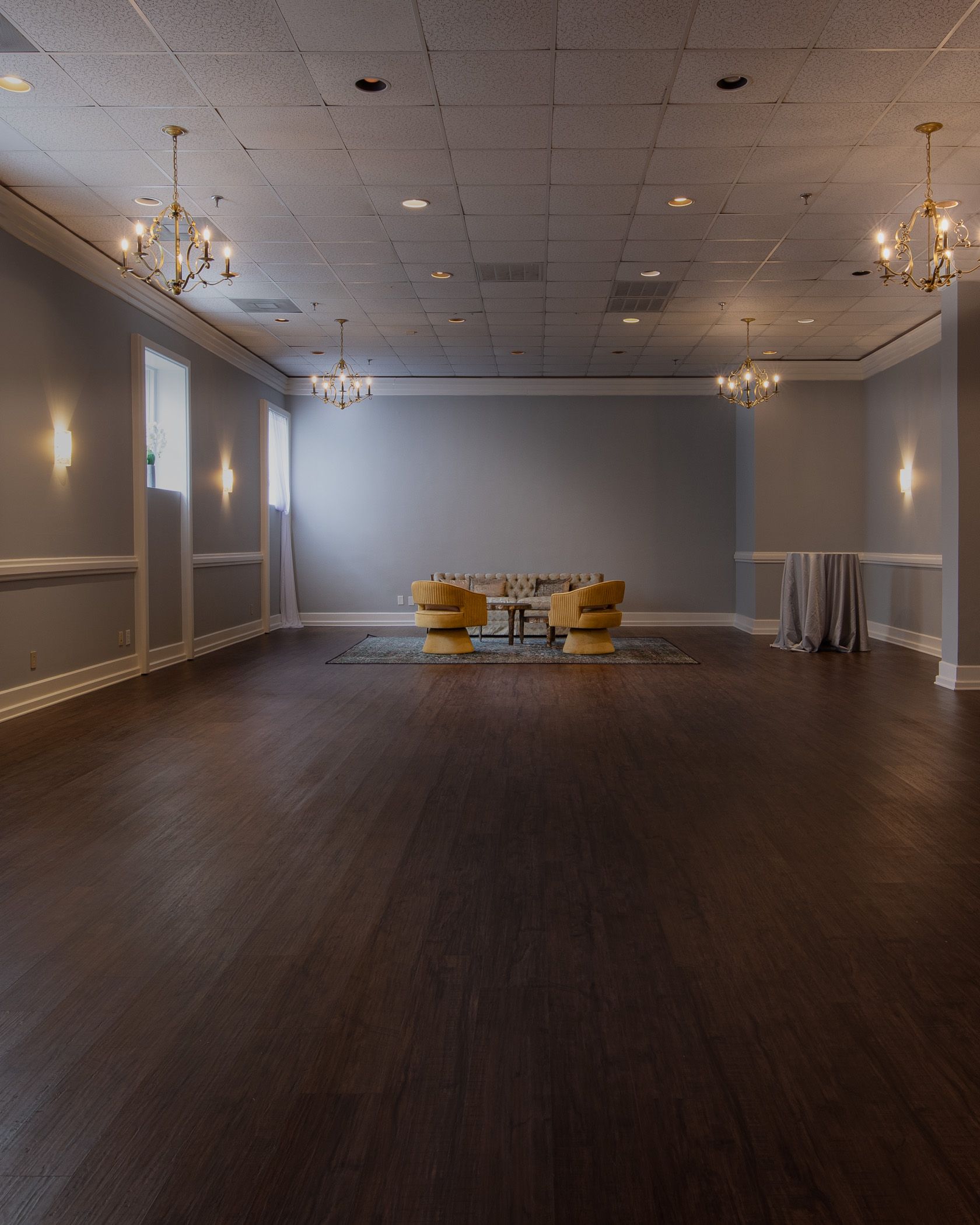 Open wooden floor with candle chandeliers and seating area against far back wall