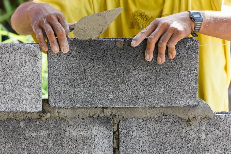 A Man Is Using A Trowel To Build A Brick Wall — Southern Bricks & Pavers In Sussex Inlet, NSW