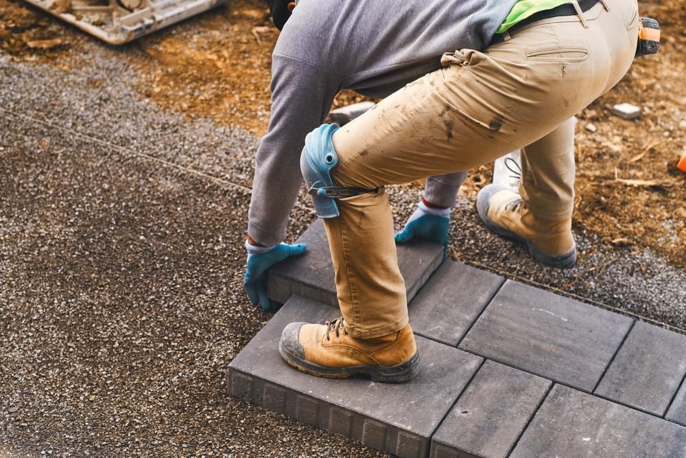 A Man Is Laying Bricks On A Sidewalk — Southern Bricks & Pavers In Sussex Inlet, NSW