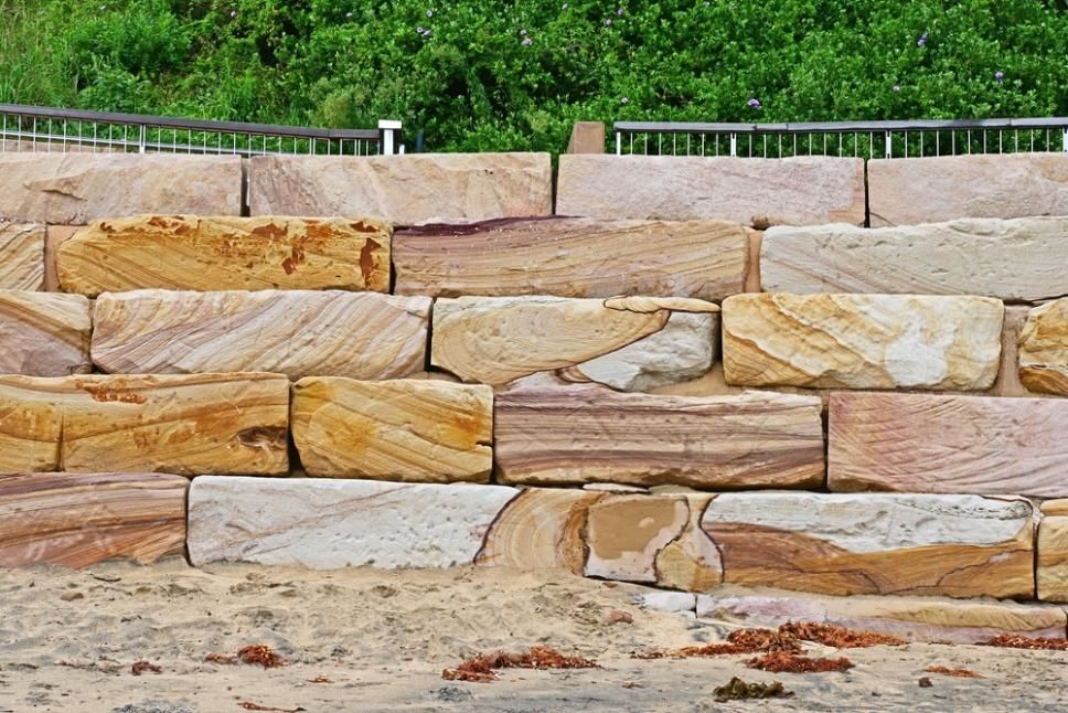 A Large Stone Wall With A Fence In The Background — Southern Bricks & Pavers In Moruya, NSW