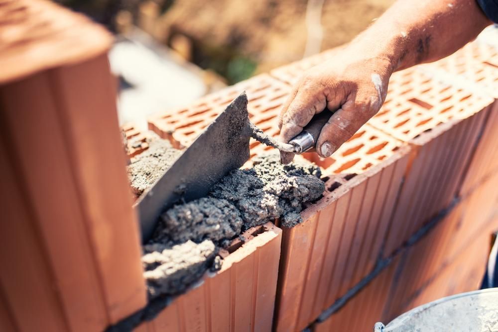 A Man Is Laying Bricks On A Wall With A Trowel — Southern Bricks & Pavers In Sussex Inlet, NSW