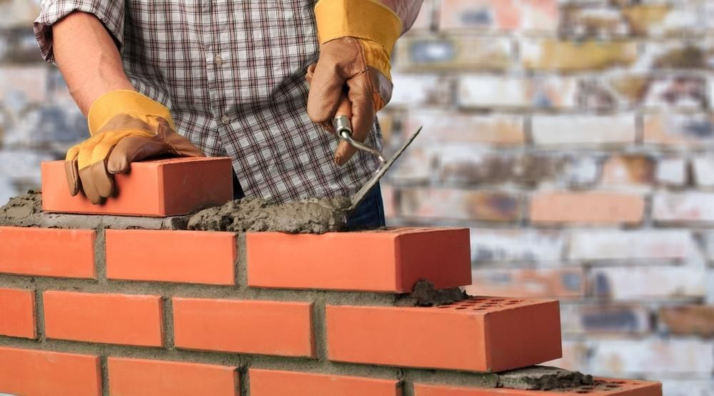 A Man Is Laying Bricks On A Brick Wall — Southern Bricks & Pavers In Moruya, NSW