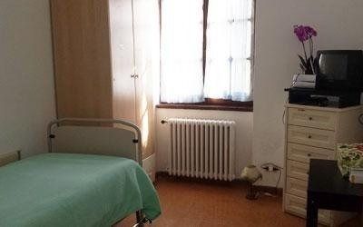 Un terapista assiste una persona nell'esecuzione di esercizi di fisioterapia utilizzando piccoli manubri, mentre si trova in piedi in una stanza illuminata.