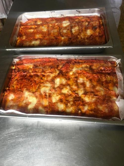 Due vassoi rettangolari di metallo pieni di lasagne appena sfornate, ricoperte di formaggio e salsa di pomodoro