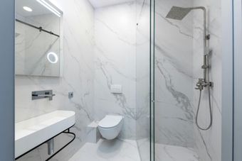 Modern white marble bathroom with a walk-in shower, floating sink, and toilet.
