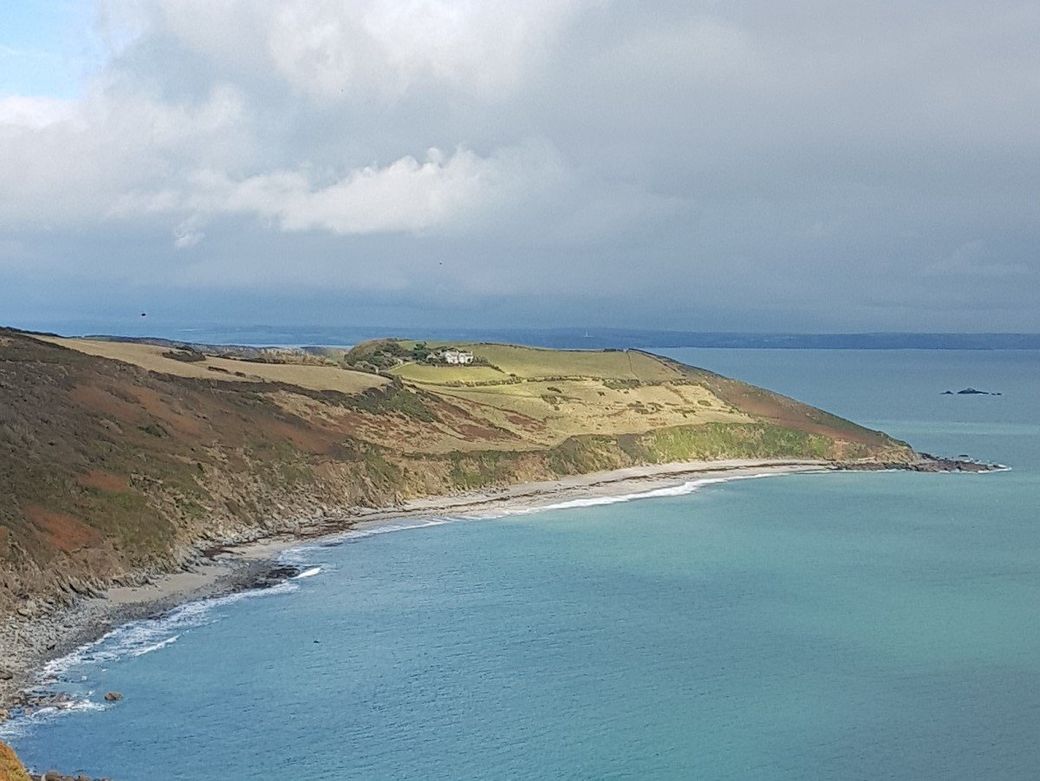 View from high cliffs to a blue bay and sandy beach backed by a green headland