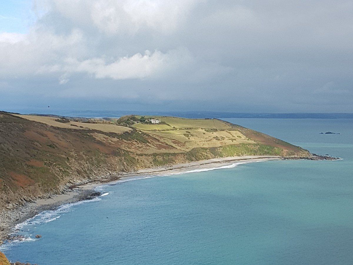 View from high cliffs to a blue bay and sandy beach backed by a green headland