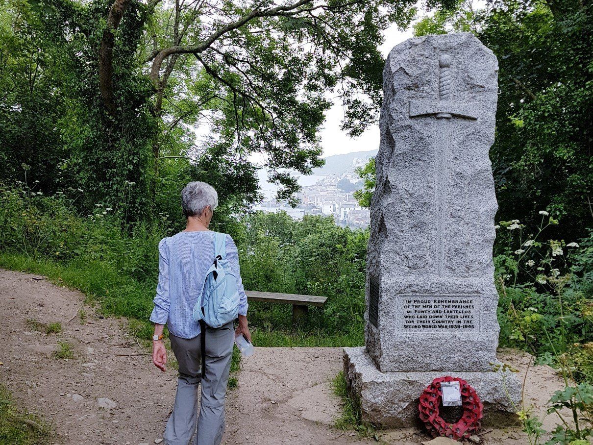 A walker contemplating the granite war memorial by the Hall Walk path flanked by tall trees