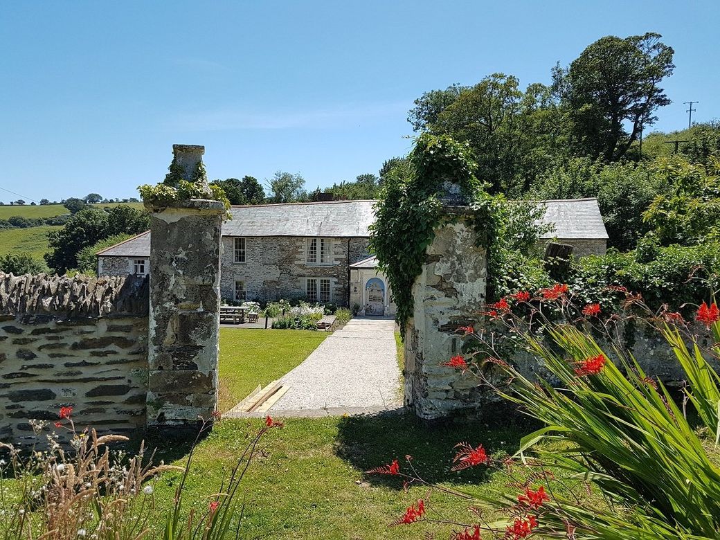 Seventeenth century stone manor house seen between tall gate posts across a green lawn