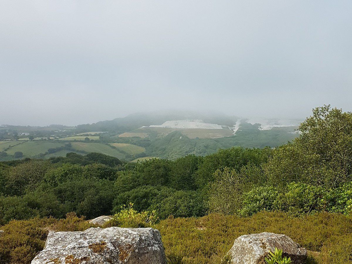 Long view over wooded valleys to a misty moorland top with china clay pits