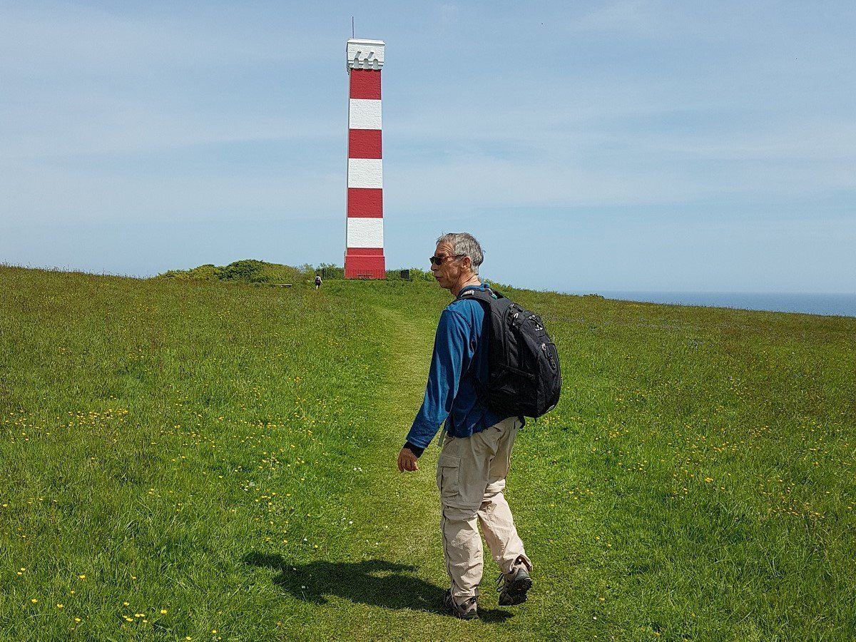 A red and white striped shipping marker tower with a walker approaching across the clifftop path