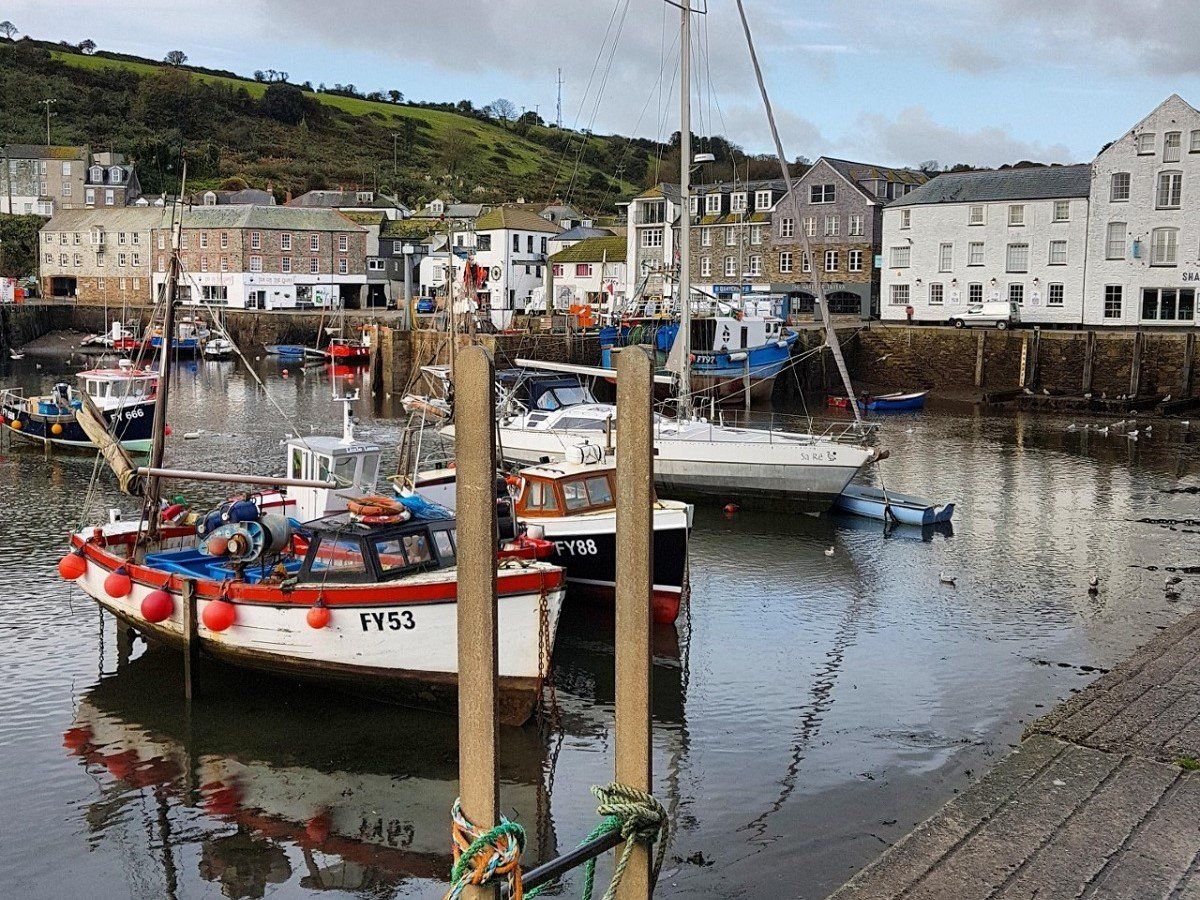 Colourful boats moored in Mevagissey harbour with reflections on the water