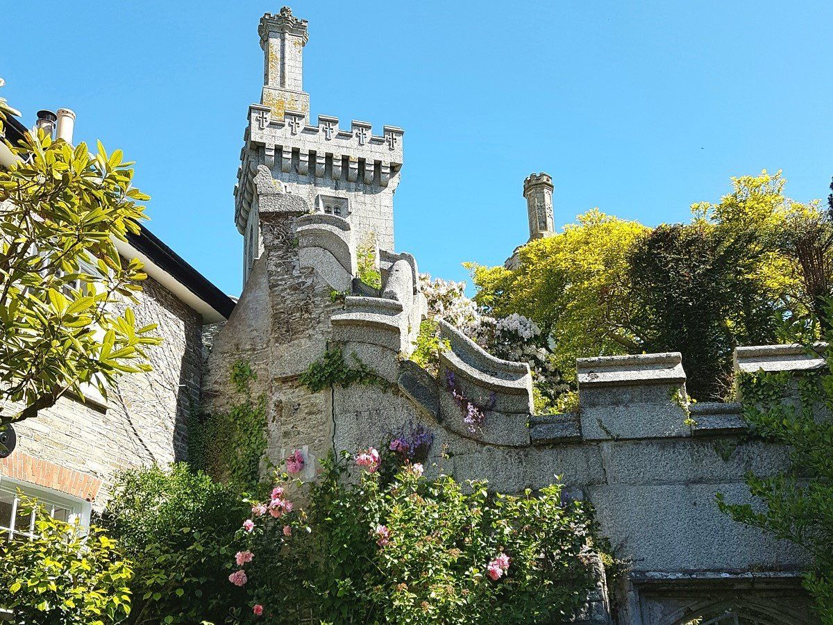 A tall tower and crenellated walls with lush flowering shrubs and a blue sky