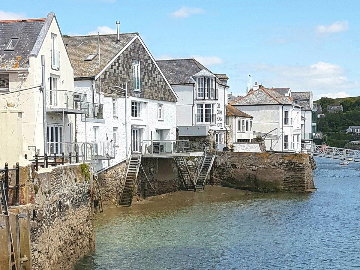 Old white-painted buildings next to the river at low tide by Town Quay in Fowey