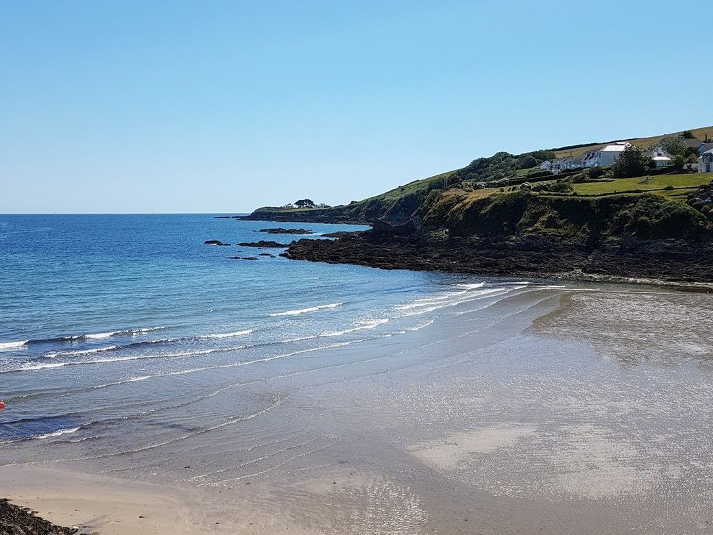 Sandy beach with blue sea and waves rolling in and a rocky headland beyond