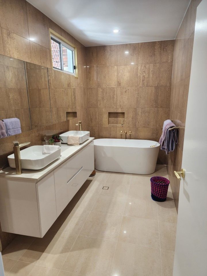 Modern beige bathroom with double vanity, freestanding tub, window, and tiled walls