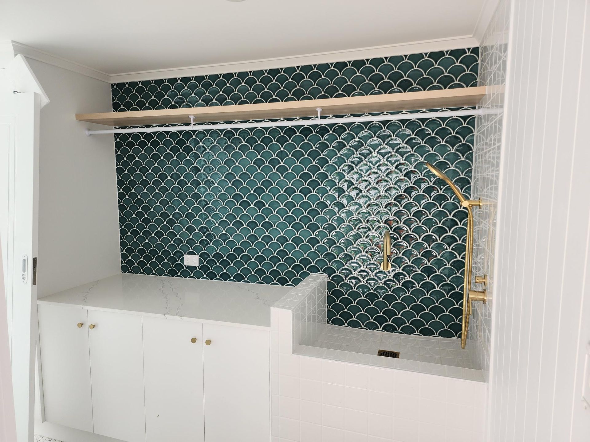 White kitchen alcove with teal tile backsplash, wood shelf, gold fixtures, and white cabinets