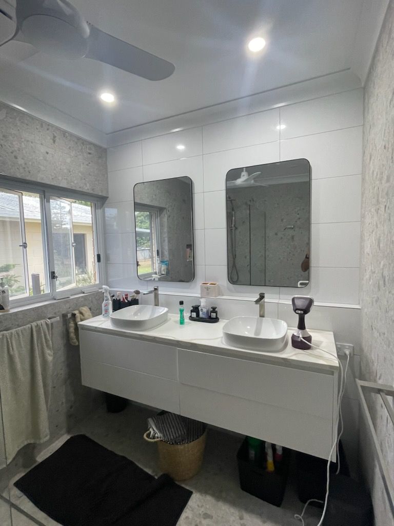 Modern bathroom with double sinks, large mirrors, white tile walls, and a shower curtain by a window.