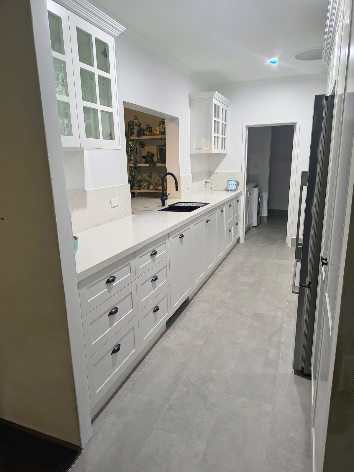 Bright white kitchen with long counters, cabinets, sink, and stainless appliances in a narrow hallway view