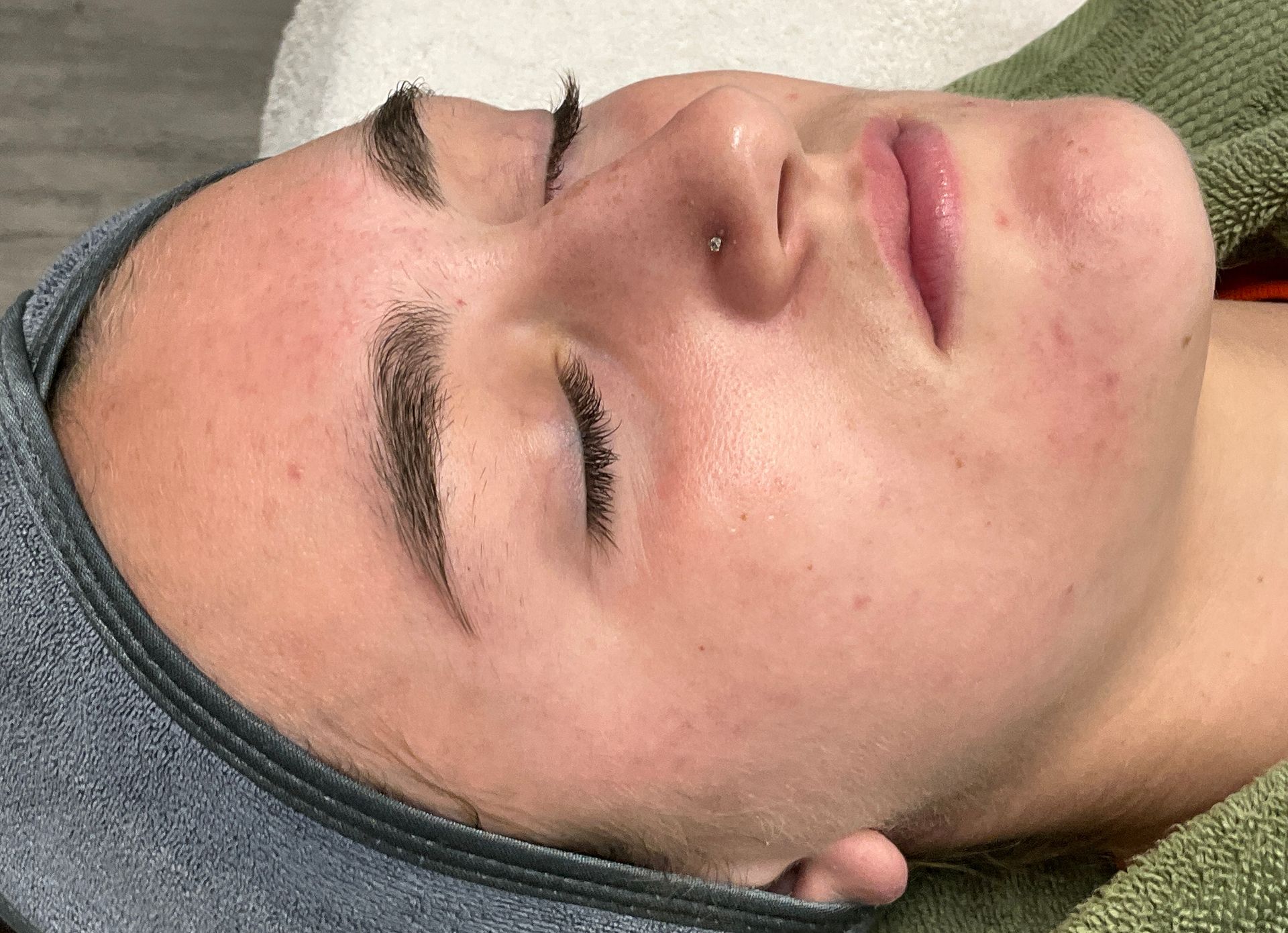 A woman with a nose ring and closed eyes lies with a gray headband and a green towel.