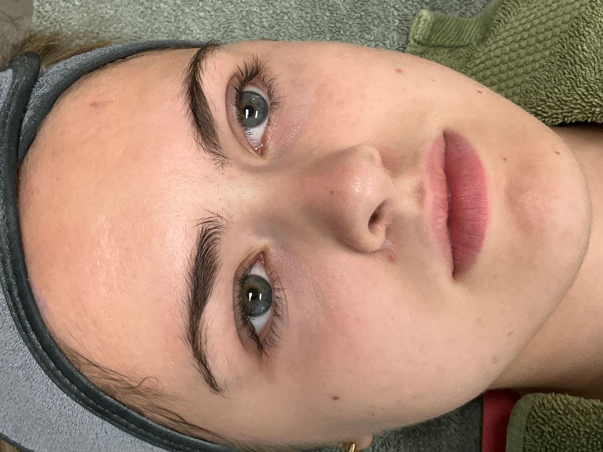 Woman's face with full eyebrows and light pink lips. Light skin, looking up with green eyes, towel around head.