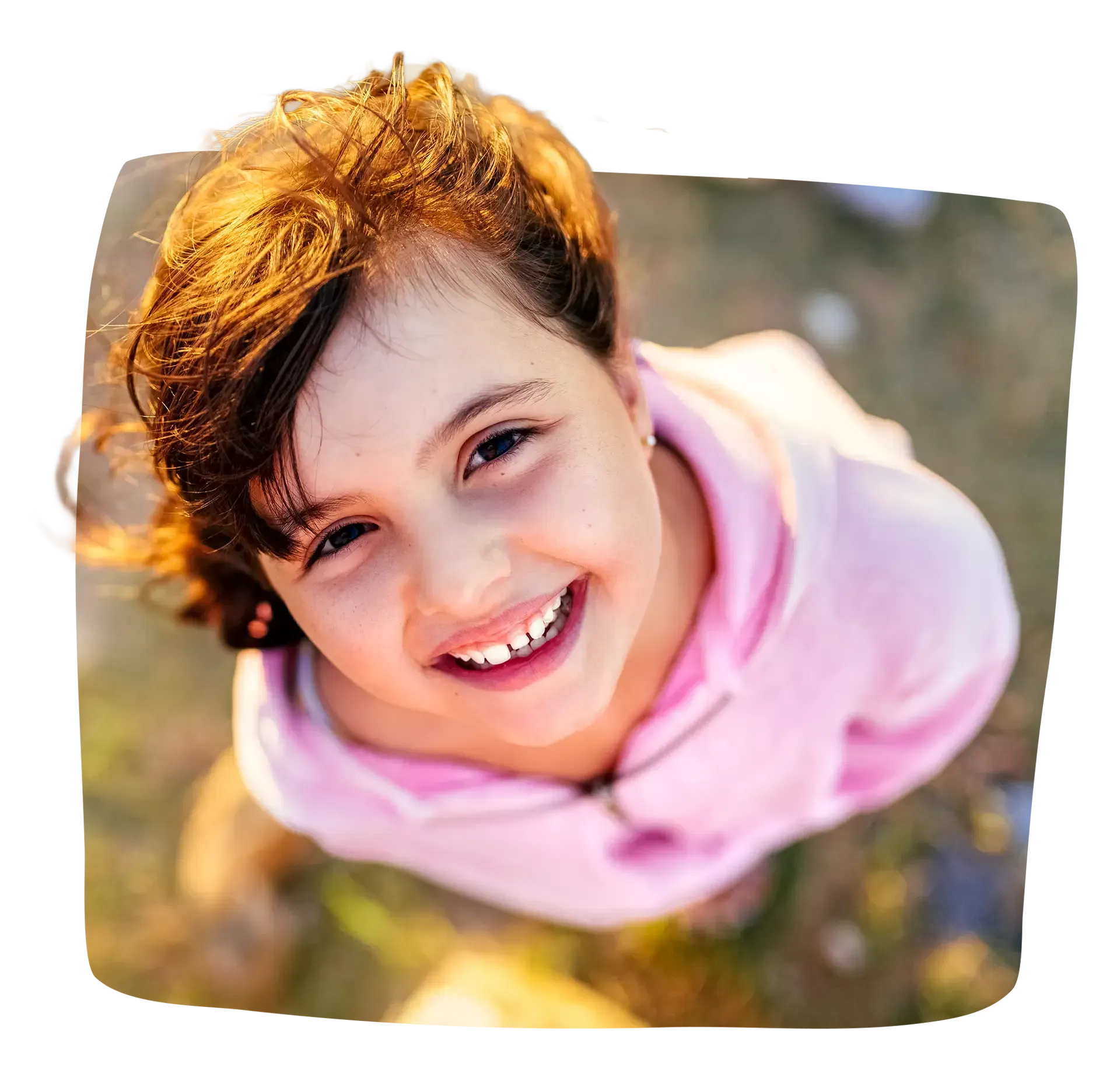 Smiling child in a pink hoodie looks up at the camera.