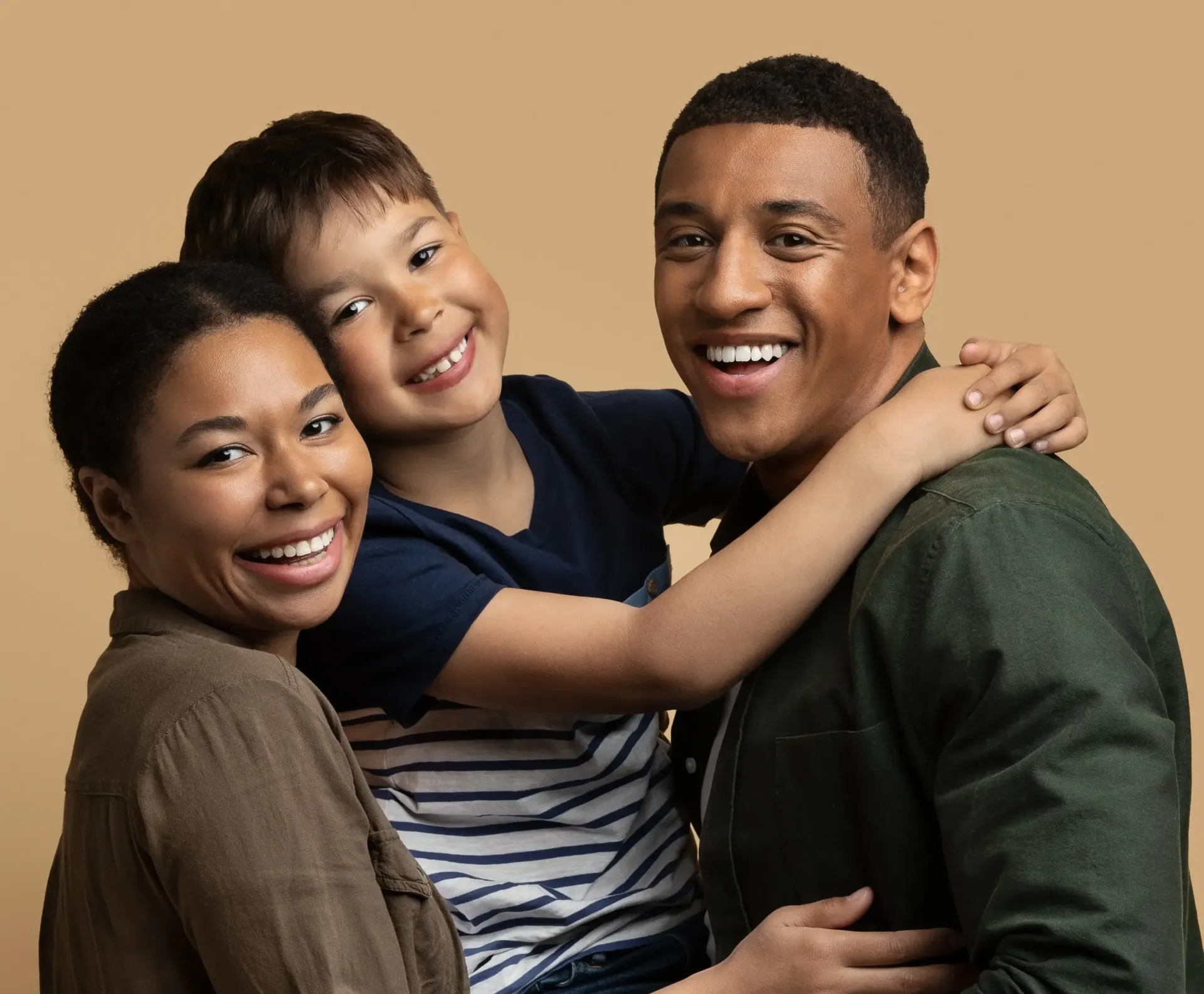 Woman hugging and laughing with a smiling child indoors; neutral background.