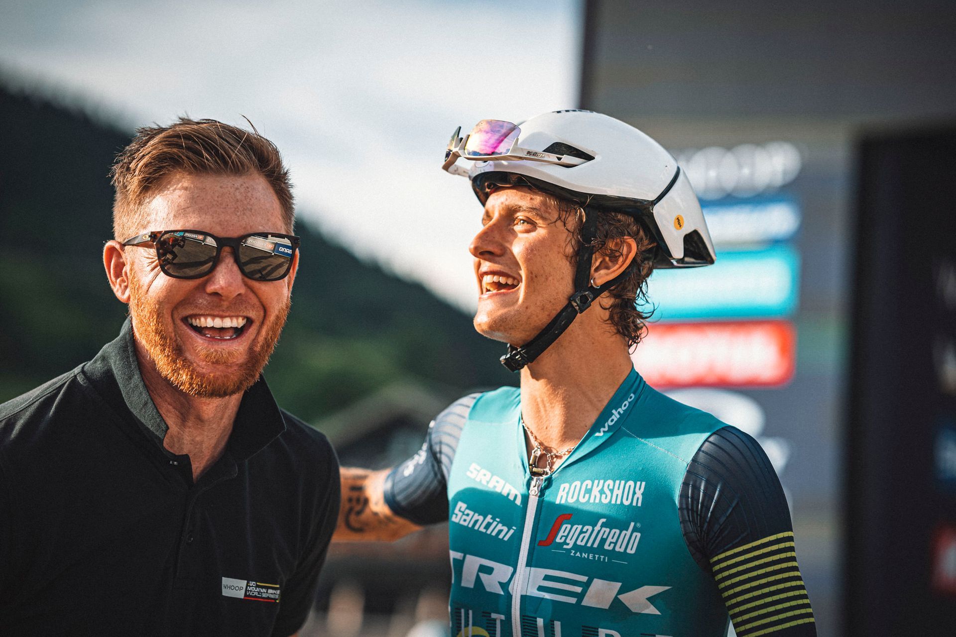 A man wearing a helmet is standing next to another man wearing sunglasses.