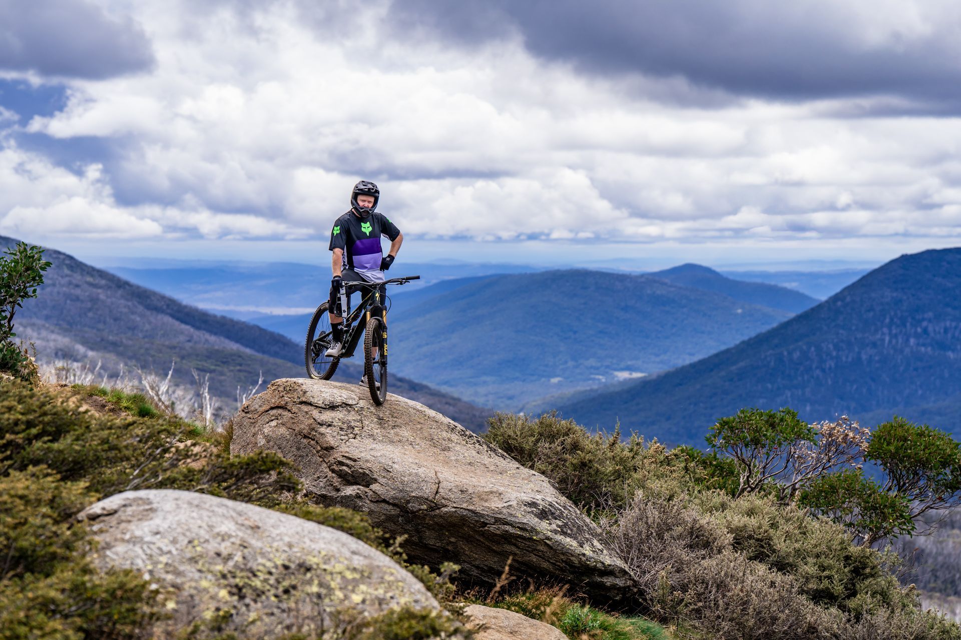 A man is holding a bicycle upside down in a grassy field.