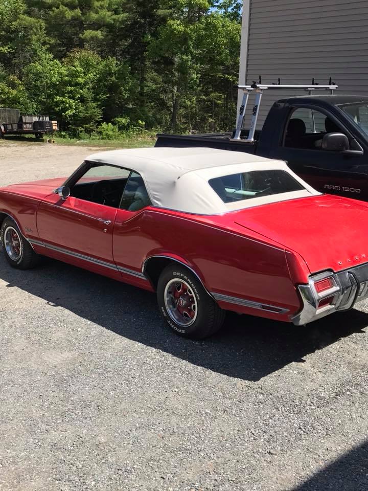 A red car with a white top is parked in a parking lot next to a truck.