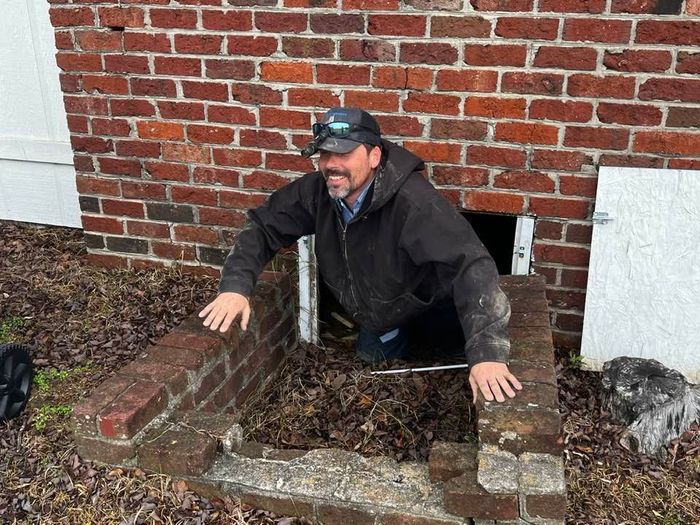 A man is crawling out of a hole in a brick wall.