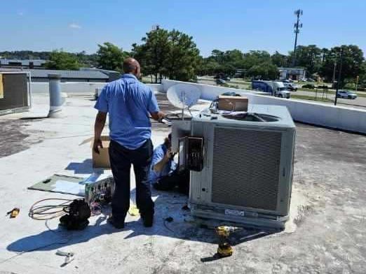 A man is working on an air conditioner on the roof of a building.