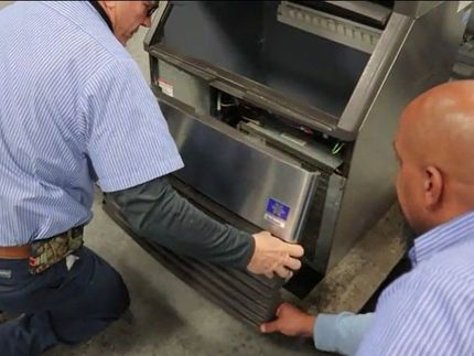 Two men are working on a stainless steel refrigerator.