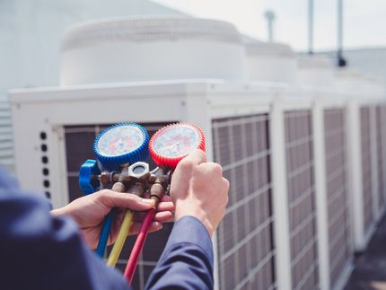 A man is holding a couple of gauges in front of an air conditioner.